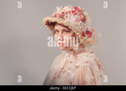 Les modèles de jeunes femmes élaborent un chapeau de fleur et un haut transparent d'inspiration vintage dans un studio lumineux Banque D'Images