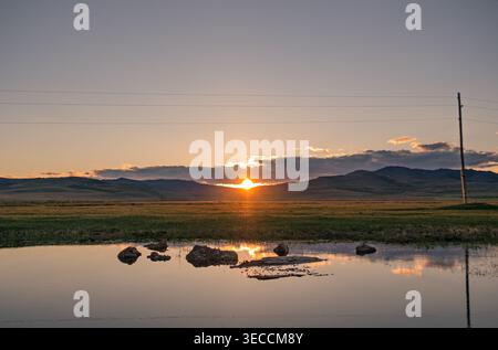 Coucher de soleil sur un lac calme avec des montagnes en arrière-plan et des reflets sur l'eau Banque D'Images