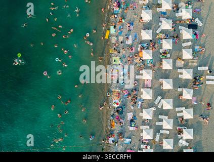 Vue aérienne d'une plage animée remplie de baigneurs profitant de l'eau chaude et du soleil sous des parasols blancs Banque D'Images
