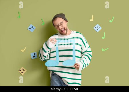 Beau jeune homme avec des notes de musique en papier chantant sur fond vert Banque D'Images