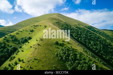 Pentes de montagne vertes et crête sinueuse sous le ciel bleu avec des nuages blancs sur une journée ensoleillée brillante Banque D'Images