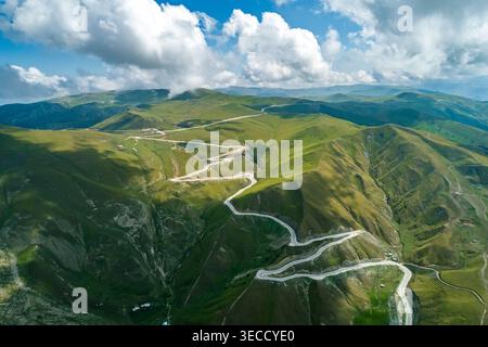 Vue panoramique sur la route de montagne sinueuse traversant des pentes verdoyantes sous un ciel lumineux Banque D'Images