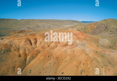 La vue aérienne capture les montagnes de l'Altaï révèlent un panorama éclatant de collines rouges et oranges sous un ciel bleu vif par temps clair Banque D'Images