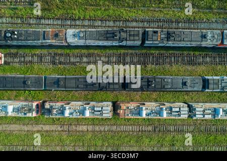 Vue aérienne de haut en bas de nombreux vieux trains abandonnés assis sur de nombreuses voies dans un grand dépôt ferroviaire vert pendant la journée Banque D'Images