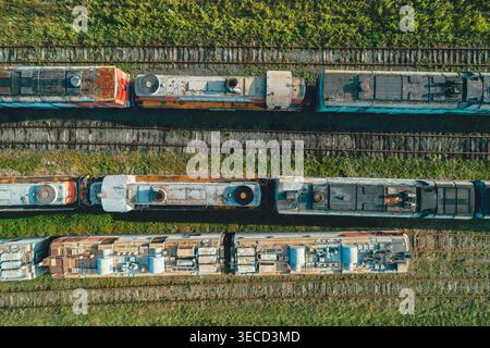 Vue aérienne de haut en bas de nombreux vieux trains abandonnés assis sur de nombreuses voies dans un grand dépôt ferroviaire vert pendant la journée Banque D'Images