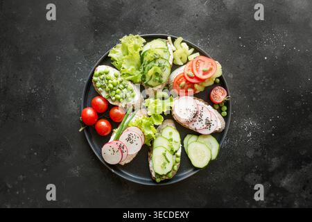 Différents sandwichs végétaliens avec légumes, radis, céleri, tomate, le pain de seigle sur fond noir. Haut vew. Amuse-gueule pour partie. Mise à plat. Banque D'Images