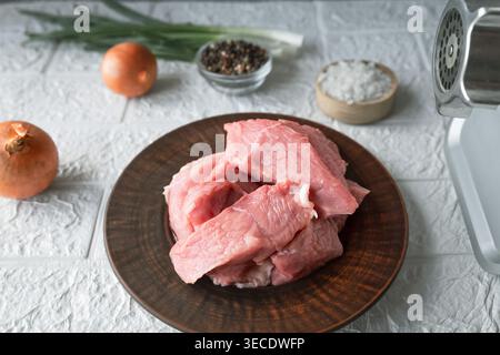 Morceaux de viande de porc crue avec des épices oignon et hachoir sur la table de cuisine pour la préparation de la cuisson Banque D'Images