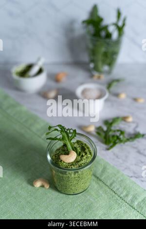 Vue de face du pesto fait de roquette et de noix de cajou stylisé sur tissu vert avec des herbes fraîches Banque D'Images