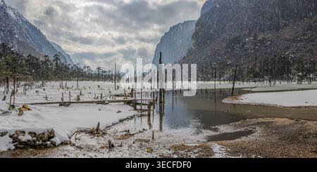 Le Sangestar Tso, vallée de montagne enneigée avec forêt morte inondée et souches d'arbres sous un ciel nuageux spectaculaire Banque D'Images