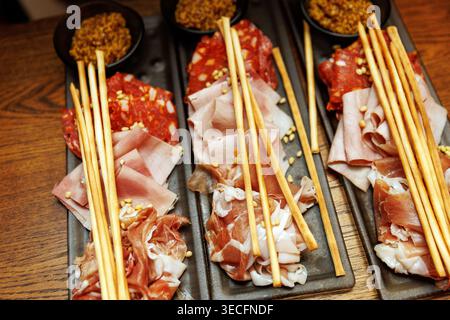 Élégant présentoir de restauration avec de fines tranches de jambon et de salami garni de pignons de pin et de grissini croustillant. Banque D'Images