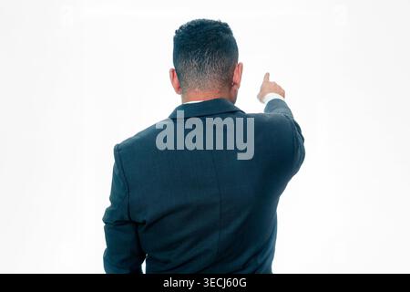 Vue arrière d'un homme indonésien en costume noir pointant son doigt vers l'avant pour indiquer une direction ou une vision, isolé sur fond blanc. Banque D'Images