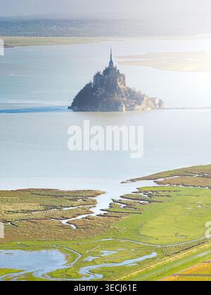 Vue aérienne de l'abbaye historique du Mont Saint-Michel s'élevant de la mer entourée de marais salants côtiers et d'eaux calmes sous la douce lumière brumeuse du Mont Banque D'Images