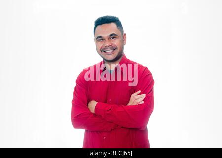 Portrait d'un homme indonésien souriant portant une chemise rouge, debout les bras croisés, exprimant la confiance et le succès sur un fond blanc. Banque D'Images