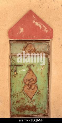 Gros plan d'une porte rustique verte altérée avec des ferronneries ornées et de la peinture écaillée sur un vieux bâtiment. Banque D'Images
