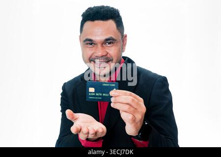 Portrait d'un Indonésien amical en costume noir tenant et présentant une carte de crédit vers l'objectif avec un sourire, isolé sur un fond blanc Banque D'Images