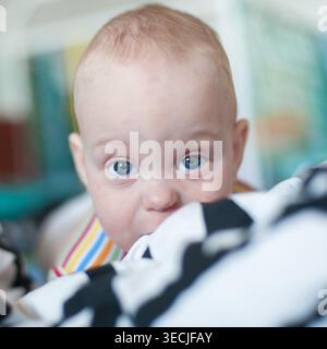 Les yeux bleus brillent de curiosité lorsqu'un bébé regarde derrière des couvertures douces. Le cadre confortable rayonne de chaleur, ce qui en fait un après-midi délicieux Banque D'Images