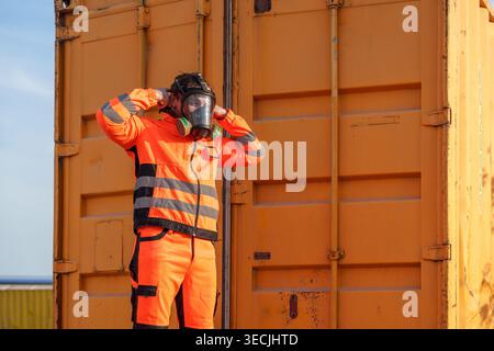 Un travailleur caucasien mi-adulte ajuste un masque respiratoire en expédiant des conteneurs pour la formation à la sécurité des matières dangereuses, la protection industrielle et l'environnement toxique p Banque D'Images