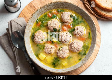 Soupe aux boulettes de viande copieuse dans un bol garnie de légumes et d'herbes vertes. Soupe de boulettes de viande au poulet maison avec des légumes verts de printemps. Banque D'Images