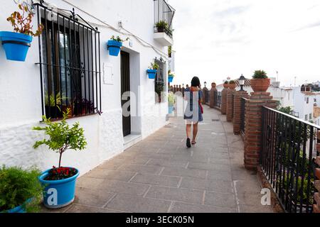 Femme marchant le long de la rue blanche du village avec des pots de fleurs Banque D'Images