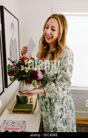 Femme d'âge moyen souriante tenant des fleurs et une note de lecture Banque D'Images