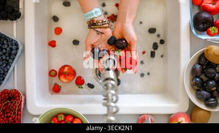 Femme lavant des baies, des prunes, des fraises, des groseilles et des pêches au-dessus d'Un évier avec Une vue descendante se concentrant sur les mains Banque D'Images