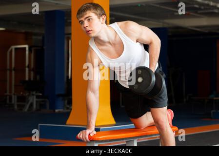 Un jeune sportif s'engage activement dans l'haltérophilie, en se concentrant sur le renforcement musculaire et l'amélioration de la force dans un cadre de gymnastique moderne, mettant en valeur le dévouement Banque D'Images