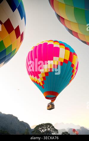 Montgolfière colorée dérivant au-dessus du paysage pittoresque de Vang Vieng, Laos, avec des montagnes calcaires et le ciel ouvert au lever du soleil, capturant une paix Banque D'Images