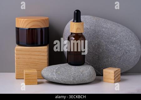 Arrangement esthétique de cosmétiques naturels, avec un pot et un flacon compte-gouttes sur des blocs de bois et une pierre lisse. Produ beauté minimaliste sur le thème du spa Banque D'Images