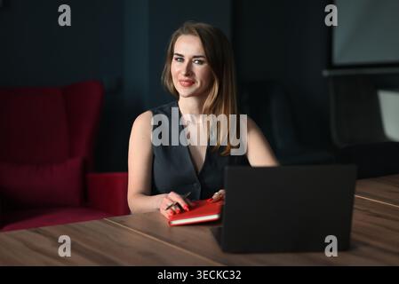Femme d'affaires confiante dans un espace de travail de bureau moderne, assise à une table en bois avec ordinateur portable et ordinateur portable, planification des tâches et gestion des projets pendant Banque D'Images