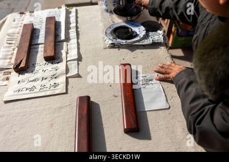 Gros plan d'une personne âgée pratiquant la calligraphie traditionnelle chinoise à une table, en utilisant de l'encre, un pinceau et des presse-papiers, capturant le patrimoine, la culture, a Banque D'Images
