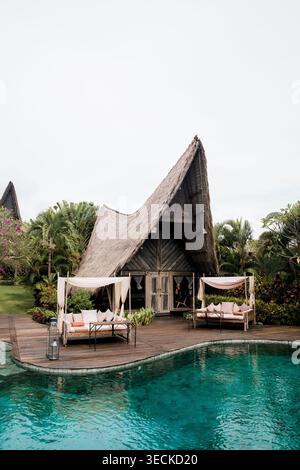 Retraite tropicale sereine à Bali Tegagaland, Indonésie avec une spectaculaire villa au toit de chaume, jardin luxuriant, lit de repos et piscine turquoise sous un Banque D'Images