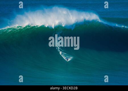 Surfeur solitaire sculpte le visage d'une vague atlantique imposante, avec un jet blanc explosif et une eau bleu profond, capturant l'énergie du surf des grosses vagues à Portug Banque D'Images