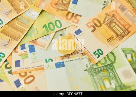 Un jeton bitcoin en or se trouve sur des billets de banque mélangés de 50 et 100 euros dans un fond d'argent en couches. Monnaie numérique et concept de finance combinant crypto et Banque D'Images