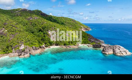 De vastes collines verdoyantes couvertes d'une végétation dense rencontrent la vaste étendue de l'océan bleu clair avec des formations rocheuses. Seychelles, Mahé. Banque D'Images