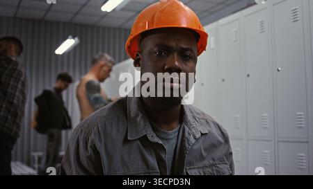 Portrait d'un travailleur afro-américain dévoué dans Orange Hard Hat, regardant en toute confiance dans la caméra avec une expression sérieuse et responsable dans la zone d'habillage. Professionnalisme dans l'industrie lourde. Banque D'Images