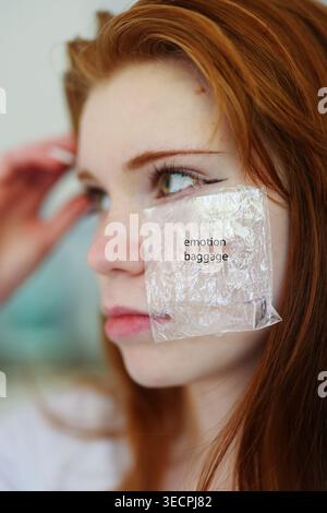 Jeune femme rousse avec autocollant en plastique disant l'émotion sur la joue, concept créatif sur les sentiments, la vulnérabilité et la perception de soi. Banque D'Images