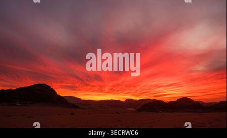 Une vue imprenable sur un coucher de soleil sur un paysage désertique, avec des teintes vibrantes de rouge et d'orange illuminant le ciel pendant l'heure dorée, créant un s. Banque D'Images