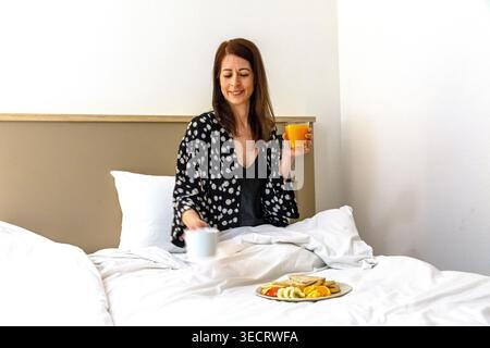 Femme appréciant la routine du matin avec le petit déjeuner au lit Banque D'Images