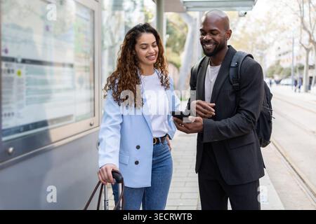 Couple d'affaires sur un voyage de travail se tient à un arrêt de transport en commun de la ville avec des bagages et des sacs à dos, vérifier un smartphone pour les directions, les déplacements et le séjour m Banque D'Images