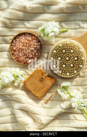 Vue de dessus de la nature morte du spa naturel avec brosse de corps en bois, savon à la main, et cristaux de sel rose spa sur tissu doux, accentué de fleurs blanches pour c. Banque D'Images