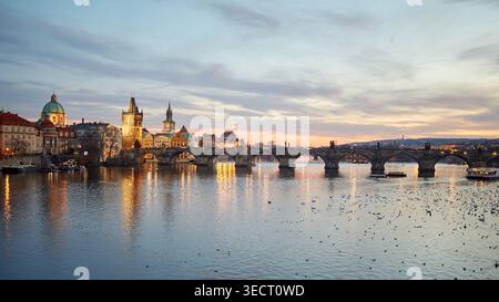 L'emblématique pont Charles de Prague est illuminé au coucher du soleil, projetant une lueur chaude sur la rivière Vltava. Architecture historique et reflets créent Banque D'Images