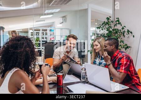 Divers collègues collaborent à une table de conférence, remue-méninges des idées avec des ordinateurs portables et des documents dans un bureau ouvert moderne, montrant le travail d'équipe, Strateg Banque D'Images