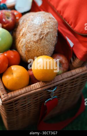 Le panier tissé contient des produits frais et du pain. Les pommes rouges, les oranges et les tomates ajoutent de la couleur. Le pain chaud repose à côté des fruits vibrants. Sac en tissu rouge ajoute co Banque D'Images