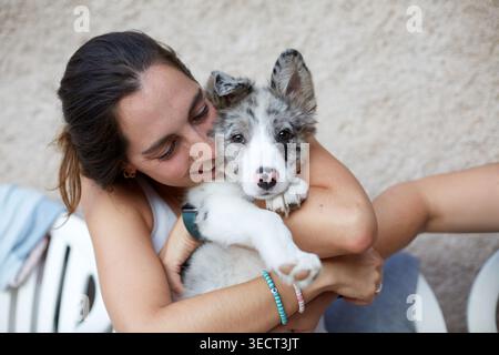 Gros plan d'une femme souriante embrassant un chiot collie de bordure moelleux avec une fourrure merle bleue. Mignon jeune chien et animal de compagnie moment de liaison, à l'extérieur en doux naturel Banque D'Images