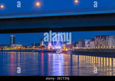 Vue nocturne de Dusseldorf le long du Rhin, avec grande roue lumineuse, bâtiments éclairés en bord de mer, et lumières de pont réfléchissant sur l'eau, capt Banque D'Images