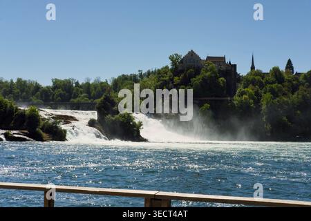 Vue panoramique sur les chutes du Rhin près de Schaffhausen, Suisse, avec une puissante cascade d'eau, la brume et un environnement verdoyant sous un environnement lumineux Banque D'Images