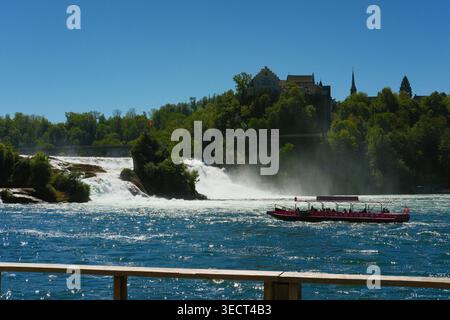 Bateau touristique rouge naviguant près des puissantes chutes du Rhin lors d'une journée d'été ensoleillée à Schaffhausen, Suisse. Destination touristique européenne pittoresque avec Banque D'Images