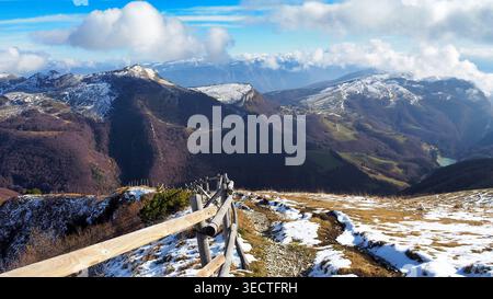 Sentier de randonnée avec clôture en bois sur le mont Baldo surplombant les sommets alpins et la vallée, Italie. Banque D'Images