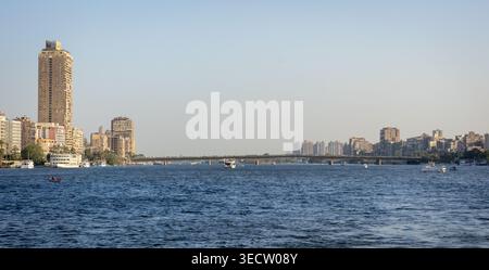 Vue sur le front de mer urbain du paysage urbain du Caire le long du Nil, avec des immeubles résidentiels de grande hauteur, un pont enjambant l'eau, et divers b Banque D'Images