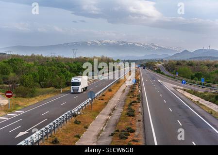 Camion conduisant sur l'autoroute avec des montagnes couvertes de neige en arrière-plan Banque D'Images